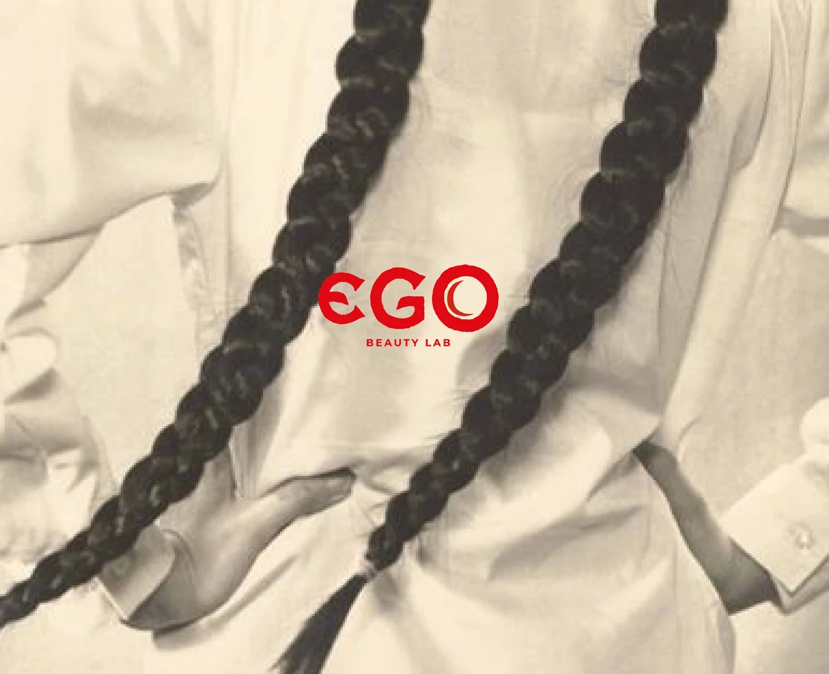 EGO red wordmark over a sepia portrait of long braids and an ivory garment